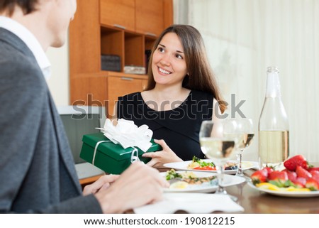 Girl giving gift  to man at table during romantic dinner in home
