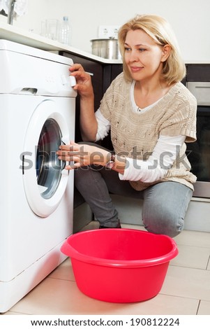 Home laundry. Happy mature woman using washing machine at home