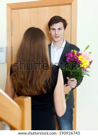 Smiling man giving flowers and gift to woman at home door