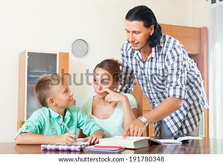 Serious couple with teenager schoolboy doing homework  in home interior