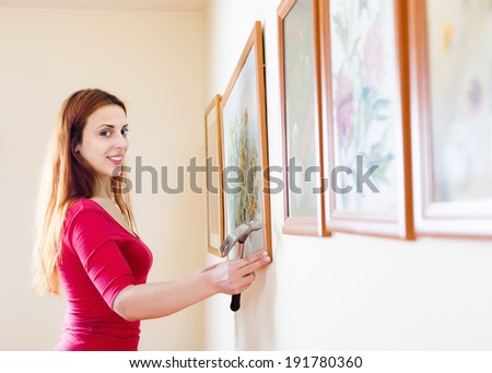 Smiling  woman hanging  picture with flowers on wall at home