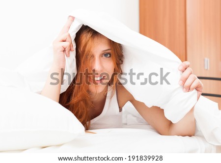 Long-haired girl under white sheet in  bed at bedroom