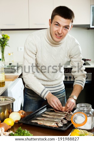 Smiling men cooking trout fish with lemon in frying pan at  kitchen