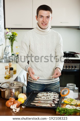 Smiling man putting pieces of onion in fish at home kitchen