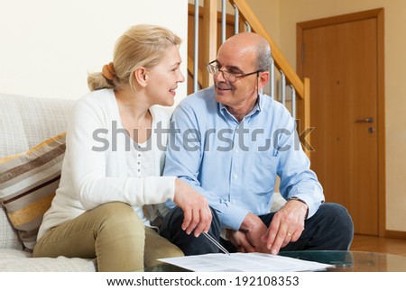 Happy elderly couple with financial documents on sofa in home interior