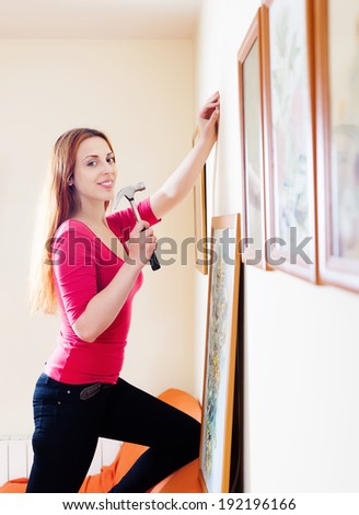 Positive  girl in red hanging  pictures in frames on wall at house