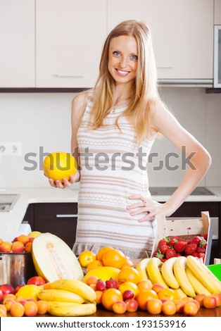 blonde long-haired woman with melon and other fruits in home kitchen