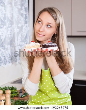 Pretty housewife in apron with cakes in kitchen