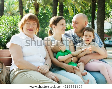 happy multigeneration family sitting on bench in sunny summer day