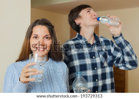 Young man and woman drinking water from a plastic bottle in the room