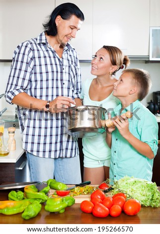 Happy man and woman with boy with fresh vegetables and greens in home kitchen
