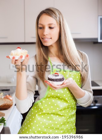 Blonde woman in apron with cakes in kitchen