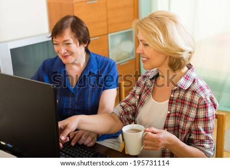 Two aged colleagues working on computer and smiling with cup of coffee in hands