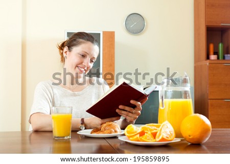young woman with book during breakfast with juice in morning at home interior