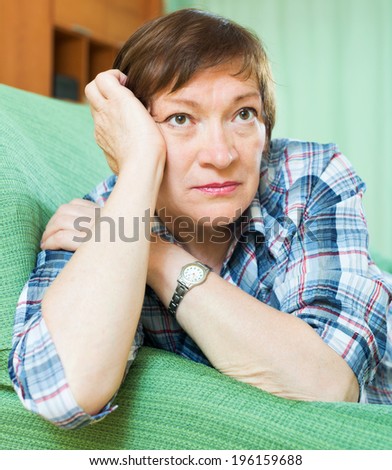 Stressed elderly female laying on her elbows and thinking  on couch