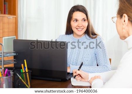 Elderly woman talking with young girl employee with laptop at office