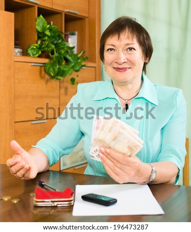 Happy mature woman with financial documents and money indoor