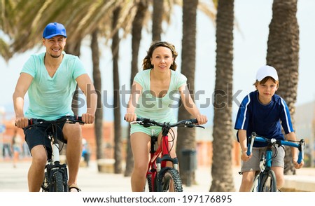 Happy family of three cycling across city in summer day