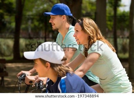 Happy couple with teenager son going by bicycles through city in summer day