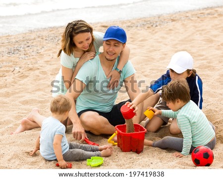 Happy parents and kids playing with sand at sea shore
