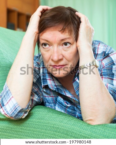 Stressed elderly woman laying on her elbows and thinking  in home interior