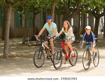 Happy family of three cycling on street road in summer day