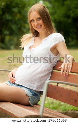 Portrait of long-haired pregnancy woman sitting in summer park
