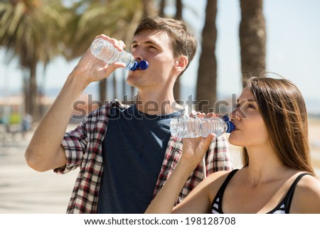 Young couple taking a refreshing drink of water from bottle outdoor