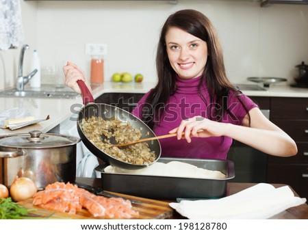 Smiling  woman cooking fish pie with salmon and vegetables in  kitchen