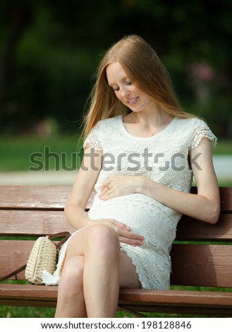 Pregnant woman sitting on bench in summer park