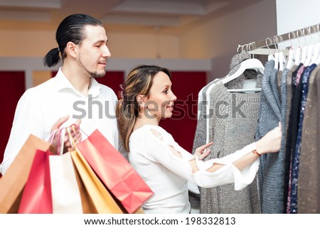 Woman and man with shopping bags choosing sweater at clothing shop