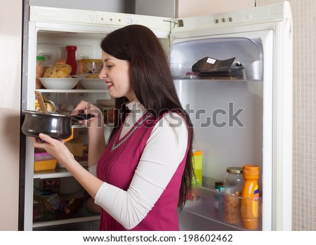 Positive brunette woman searching for something in refrigerator  at home