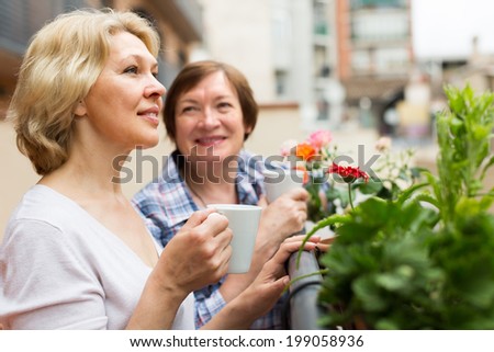 Two happy female pensioners drinking tea on balcony and smiling