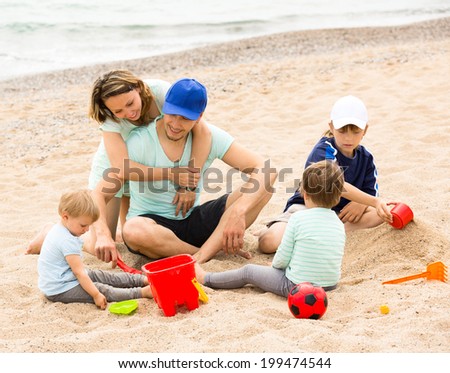 Happy parents and kids toying with sand at sea shore