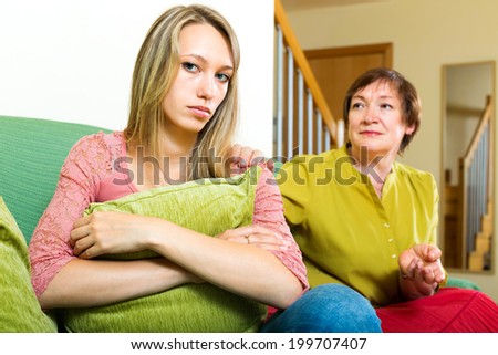 Worried mother talking to a sad daughter on the couch in the room