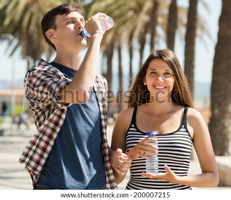 Thirsty young couple having a refreshing drink of water at sunny day
