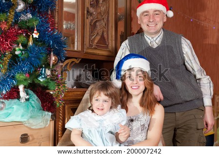 Happy family of three  in santa hats celebrating Christmas in living room