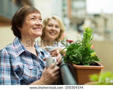 Smiling senior women staying on balcony with cup of coffee in hands