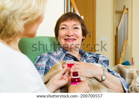 Professional retirement home employee offering  mixture to mature patient in living room