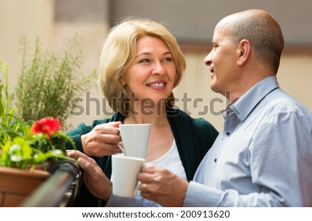 Smiling senior mature couple drinking tea and chatting on balcony