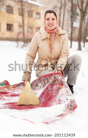 Russian woman cleans rug with snow in winter day outdoor