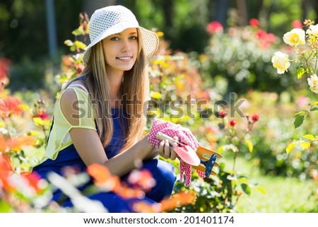 Happy smiling girl in working uniform gardening with roses in sunny day