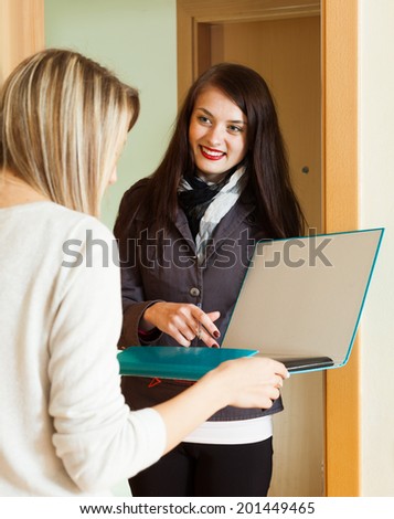 Smiling  woman in jacket polling among people at home door. Focus on blonde