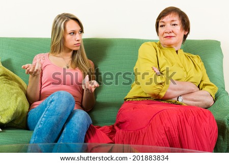 Elderly mother and adult daughter sitting on sofa and having serious conversation