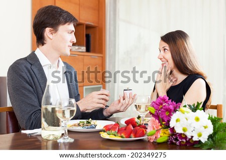 man is giving an engagement ring to his girlfriend during dinner with champagne