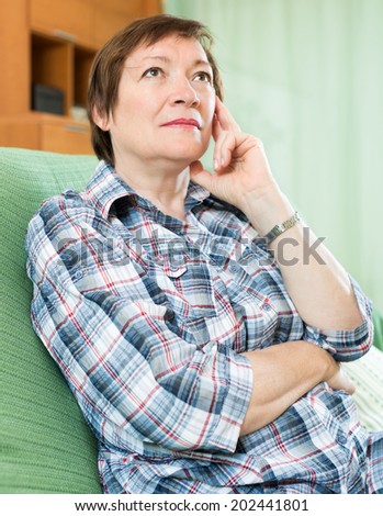 Stressed female pensioner laying on her elbows and thinking indoor