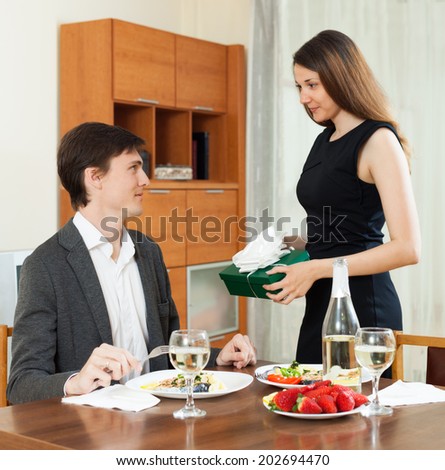 Young girl giving present box to man at table during romantic dinner
