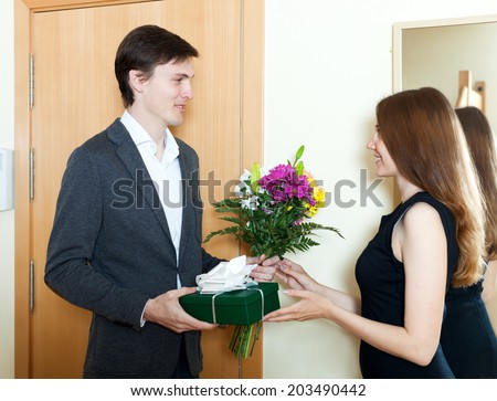 Young man giving flowers and gift to woman at home door