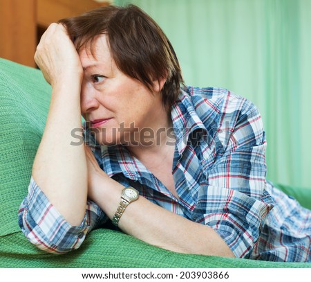 Stressed elderly woman laying on her elbows and thinking indoor