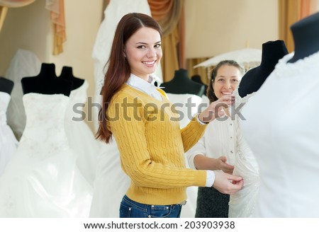 Two happy women chooses bridal outfit at  wedding boutique. Focus on bride